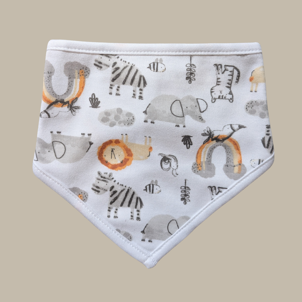 A white triangular bib with a safari-themed animal and nature print, featuring zebra, elephant, lion, and rainbow motifs in gray, black, and orange, set against a solid beige background.