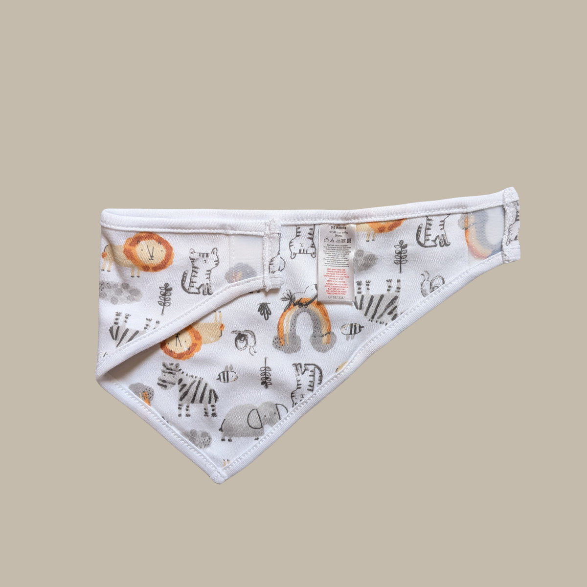 A white triangular baby bib with a playful safari-themed print of lions, zebras, rainbows, and trees in grey, orange, and black