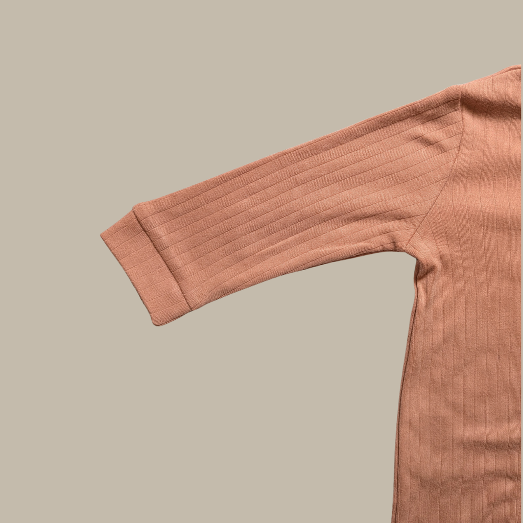 A close-up of a ribbed cotton long-sleeve top in a muted dusty rose pink, showing the sleeve cuff and shoulder seam