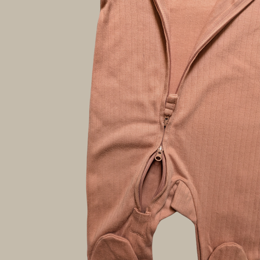 Close-up of a ribbed cotton baby jumpsuit in a dusty rose pink colour, showing the front zipper closure and leg openings