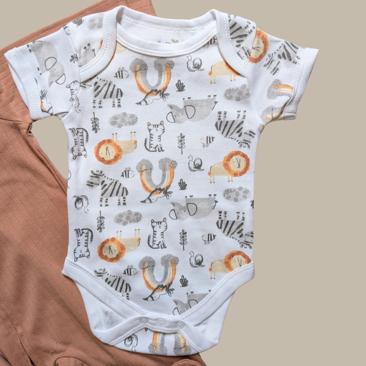 A white short-sleeve baby bodysuit with an all-over playful animal print featuring lions, zebras, insects and elephants in grey, orange, and black.
