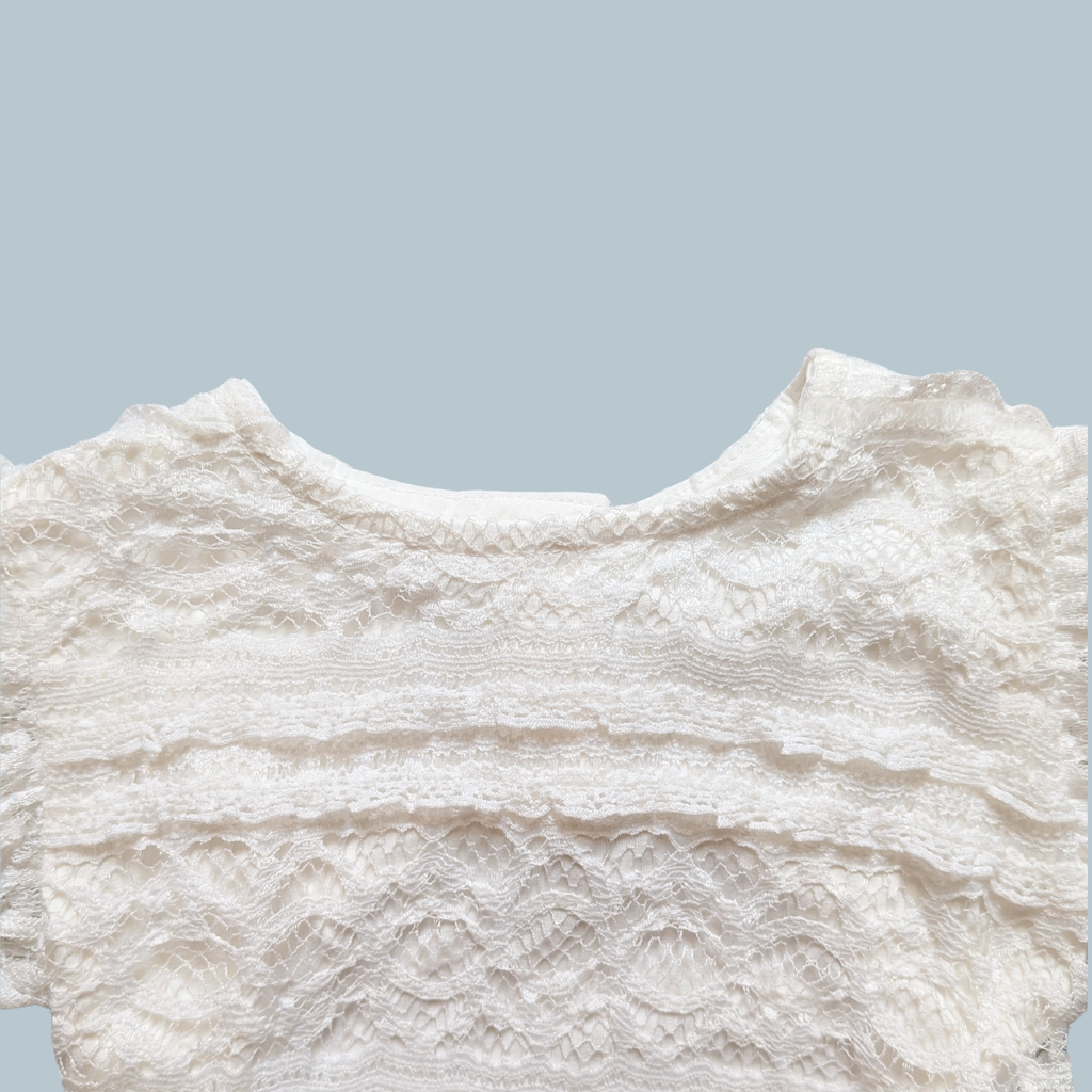 Close-up of a white lace baby bodysuit with ruffled trim and textured embroidery