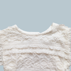 Close-up of a white lace baby bodysuit with ruffled trim and textured embroidery
