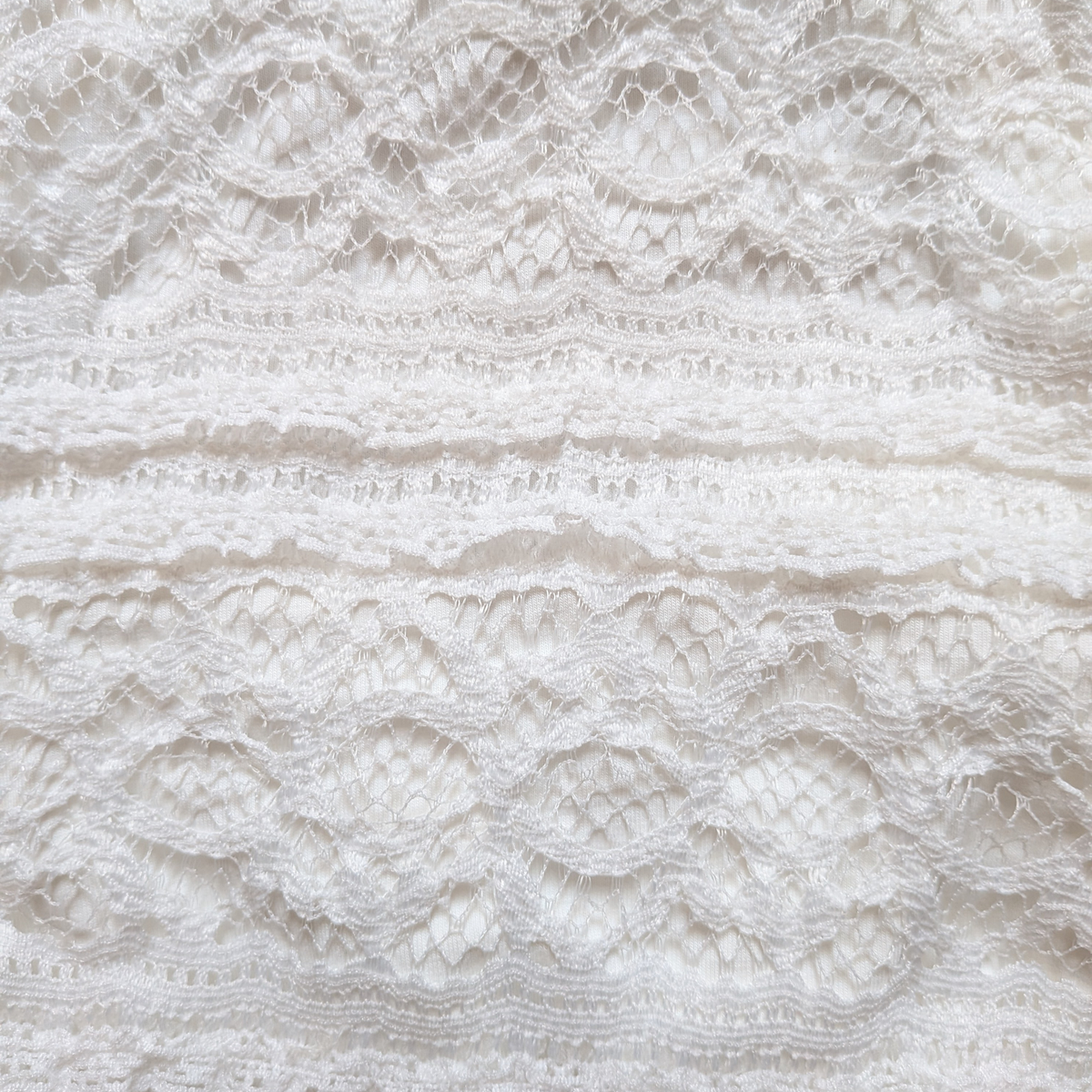 Close-up of a white lace baby bodysuit with ruffled trim and textured embroidery