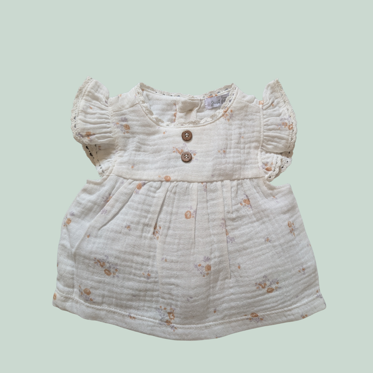 White baby top with floral patterns on a light green background