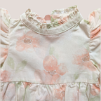 A close-up of a cotton baby romper featuring a soft, pale pink and sage green floral print on a cream-colored fabric. The romper has a ruffled mock neck, ruffled sleeves, and a ruffled waistband.