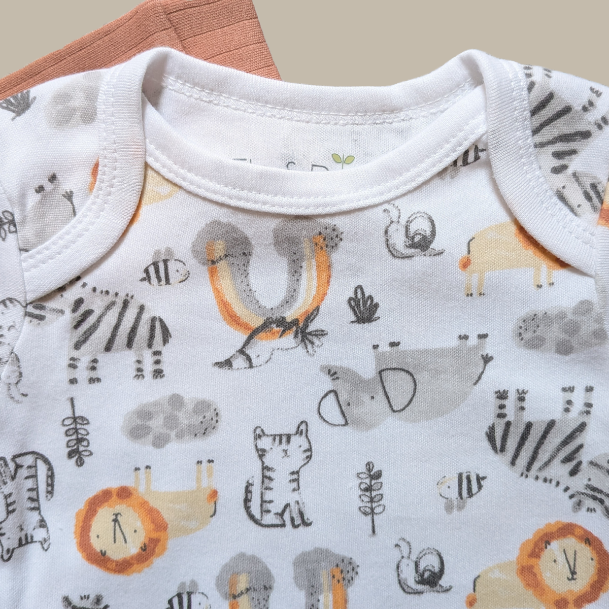 Close-up of a baby bodysuit with a white base and an all-over safari animal print including zebra, lion, insect, and bird motifs in grey, black, orange, and beige.