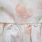 Close-up of a cotton baby romper with light pink flowers and sage green leaves  with a ruffled waistline.
