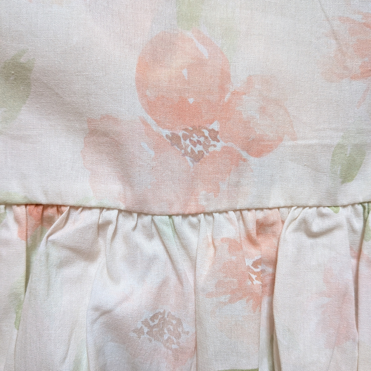 Close-up of a cotton baby romper with light pink flowers and sage green leaves  with a ruffled waistline.