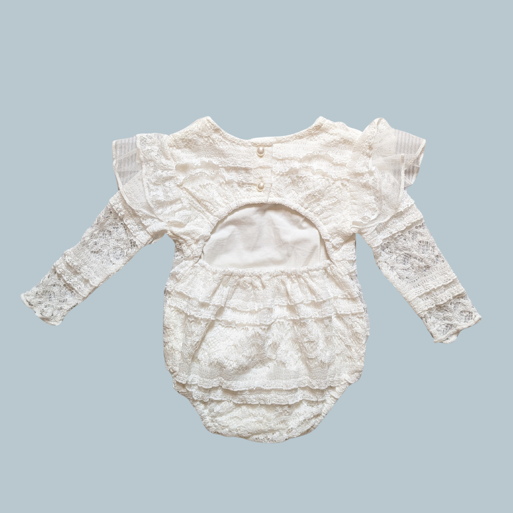 An white baby romper with long lace sleeves, ruffled lace detailing, and a buttoned neckline