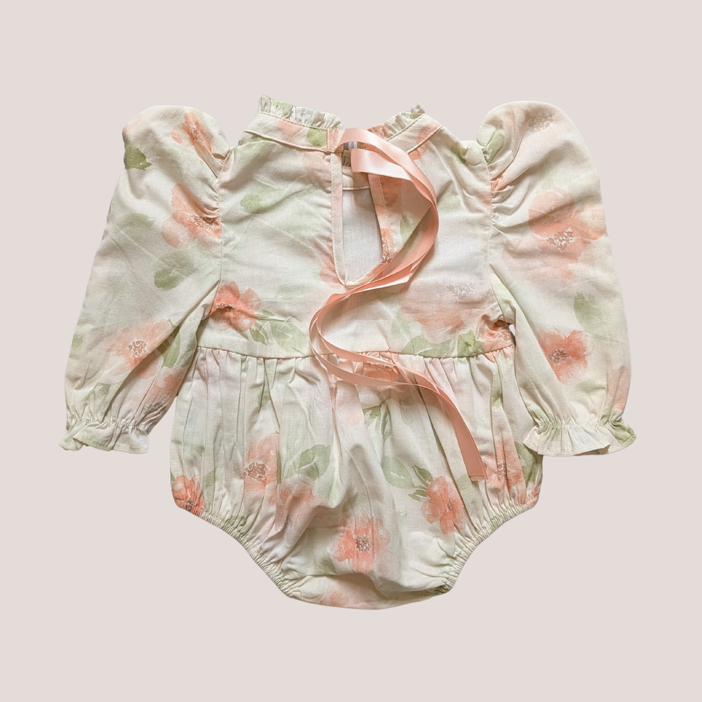 A baby long-sleeve romper in a soft, pale green floral print with pink watercolor flowers and a matching pink ribbon tie at the neckline.