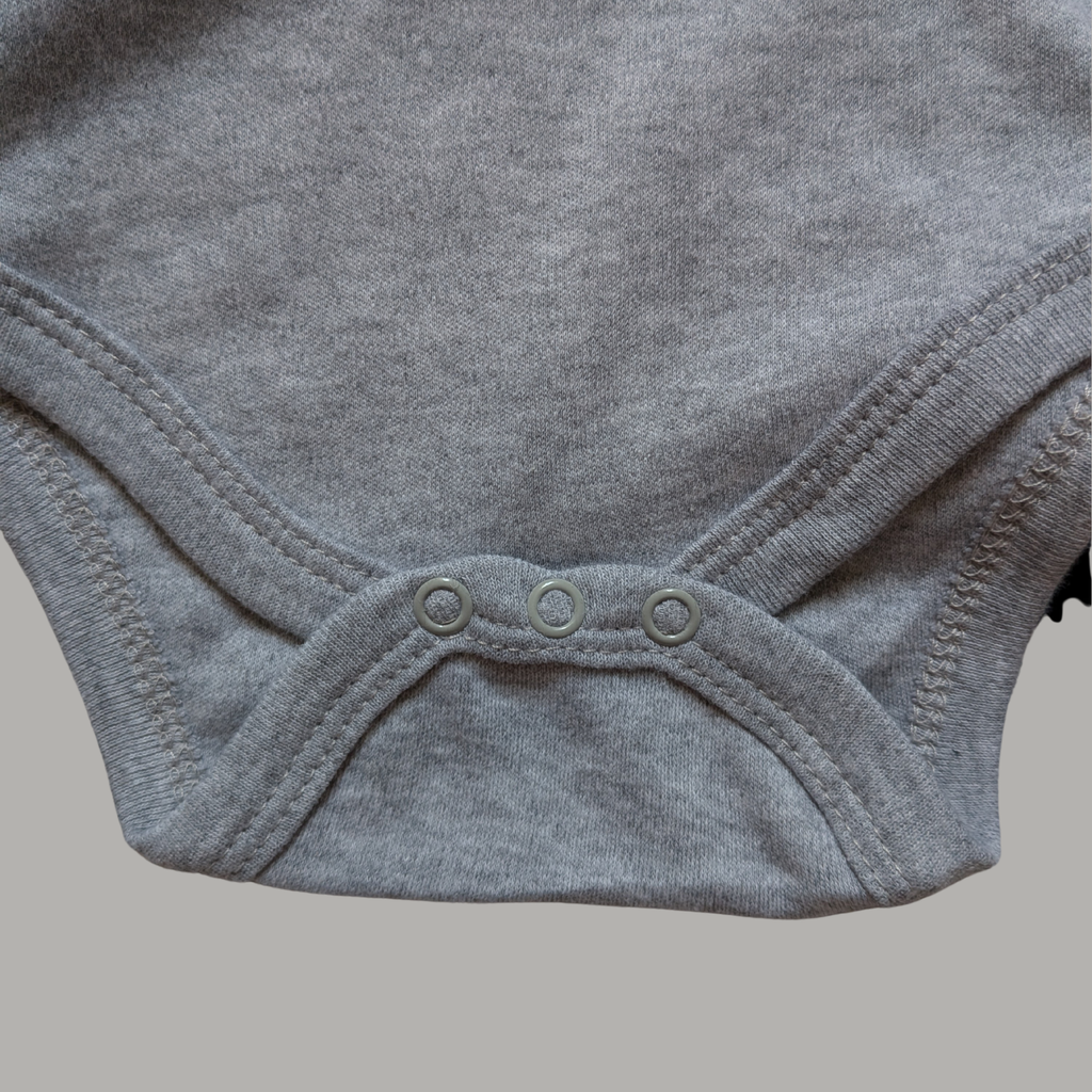 Close-up of a light grey cotton baby bodysuit showing the snap closure at the crotch with three buttons