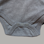 Close-up of a light grey cotton baby bodysuit showing the snap closure at the crotch with three buttons
