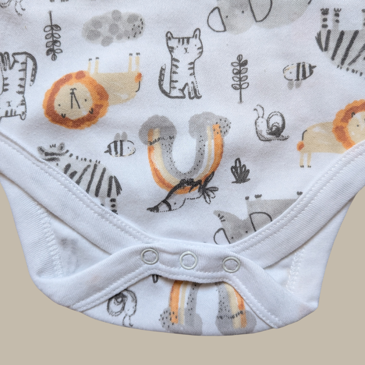 Close-up of a baby bodysuit with a white base and an all-over safari animal print including zebra, lion, insect, and bird motifs in grey, black, orange, and beige showing popper closure.