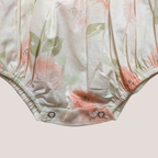 Close-up of a baby romper or bodysuit bottom with a soft floral print in peach, sage green, and cream, finished with snap closures at the leg openings.