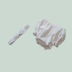 White baby bloomers and headband on a light green background